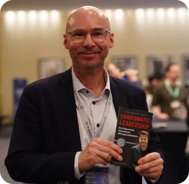 Charismatic Leadership – Praxisbuch über Führung 10 Mann Stephan H. im dunklen Anzug mit rotem Ausweis hält das Charismatic Leadership-Buch