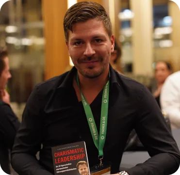 Charismatic Leadership – Praxisbuch über Führung 13 Kundenstimme Marcel H. bei einem Event mit grünem Namensschild und schwarzem Jackett