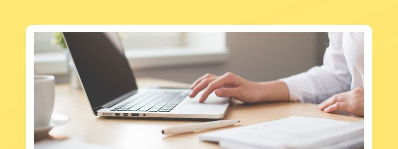 Person an Laptop-Arbeitsplatz mit Notizbuch und Stift auf gelbem Hintergrund