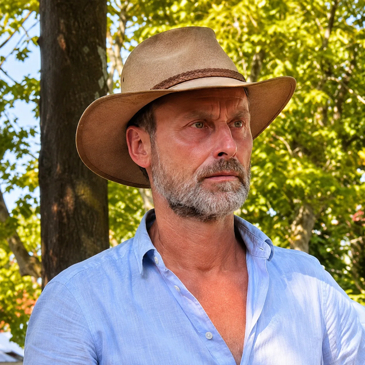 Mann mit Bart und Cowboyhut in hellblauem Hemd vor gelbgrünem Blattwerk