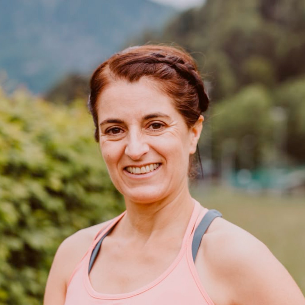 Chlorophyllkongress – Videokongress über Blattgrün von Maria Kageaki 13 Porträt einer Frau mit braunem Haar und rosa Oberteil vor unscharfem grünem und blauem Hintergrund