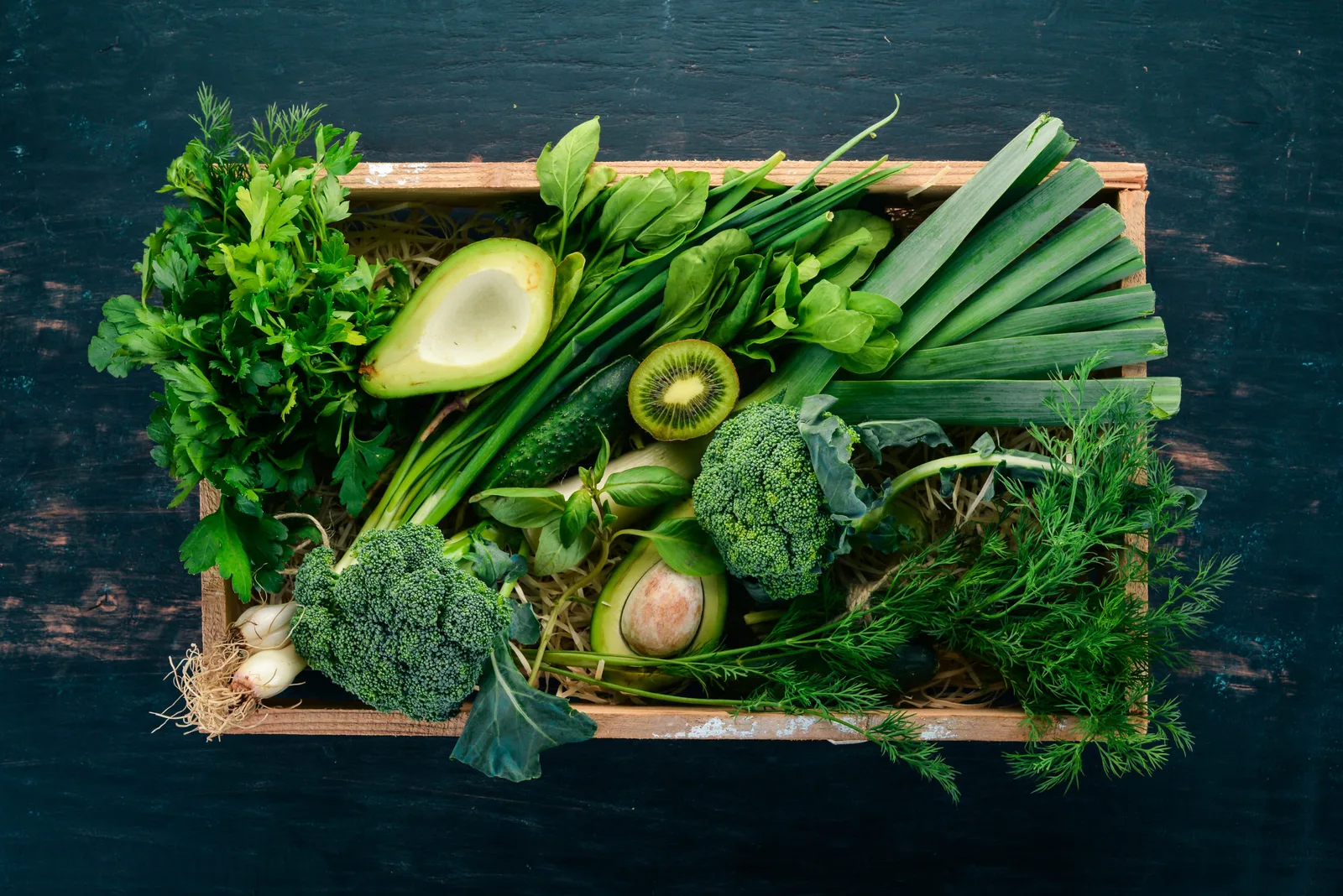 Chlorophyllkongress – Videokongress über Blattgrün von Maria Kageaki 5 Holzkorb mit frischem grünem Gemüse, Avocado, Brokkoli, grünen Bohnen und Kräutern auf dunklem Holztisch