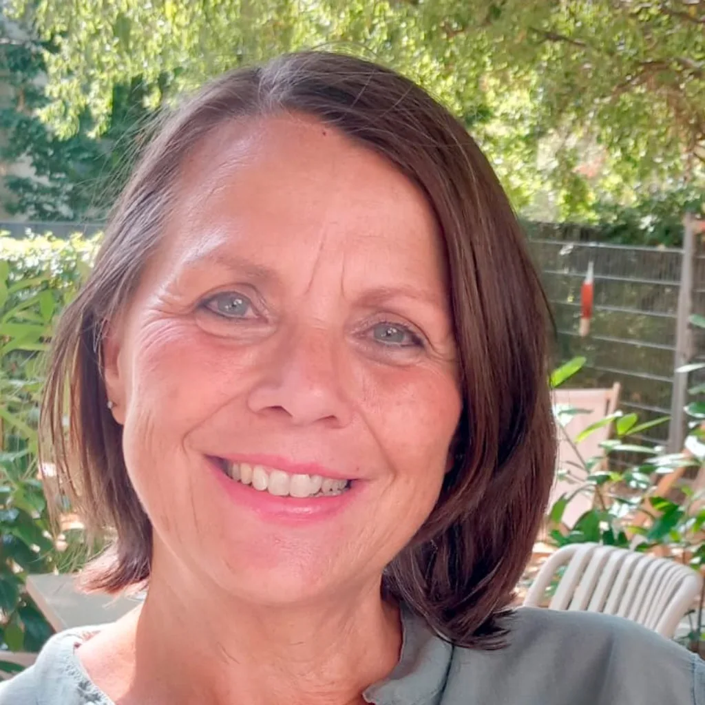 Chlorophyllkongress – Videokongress über Blattgrün von Maria Kageaki 11 Porträt einer Frau mit braunem Haar und blauem Kleid vor grüner Pflanzenhecke im Freien