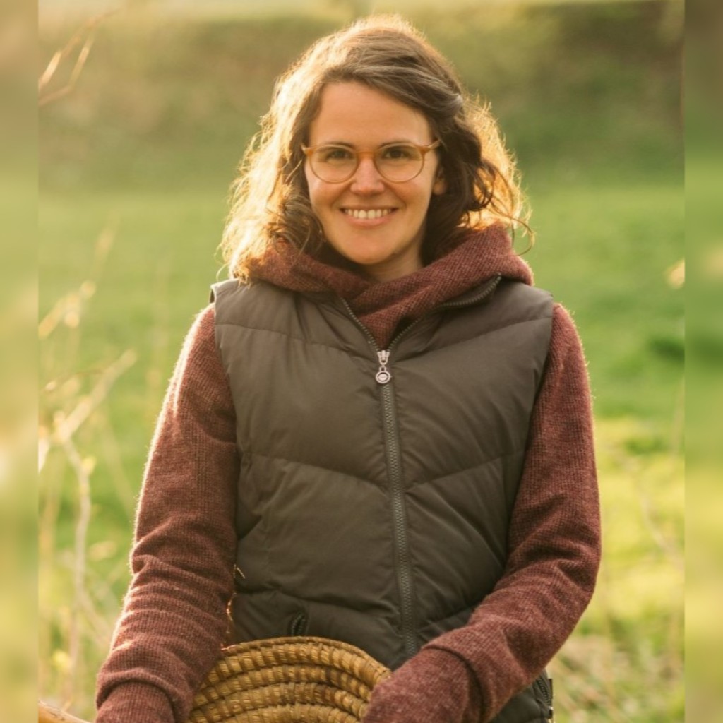 Chlorophyllkongress – Videokongress über Blattgrün von Maria Kageaki 7 Portraitfoto einer jungen Frau mit Brille, braunem Haar, lächelnd im Freien mit unscharfem grünem Hintergrund