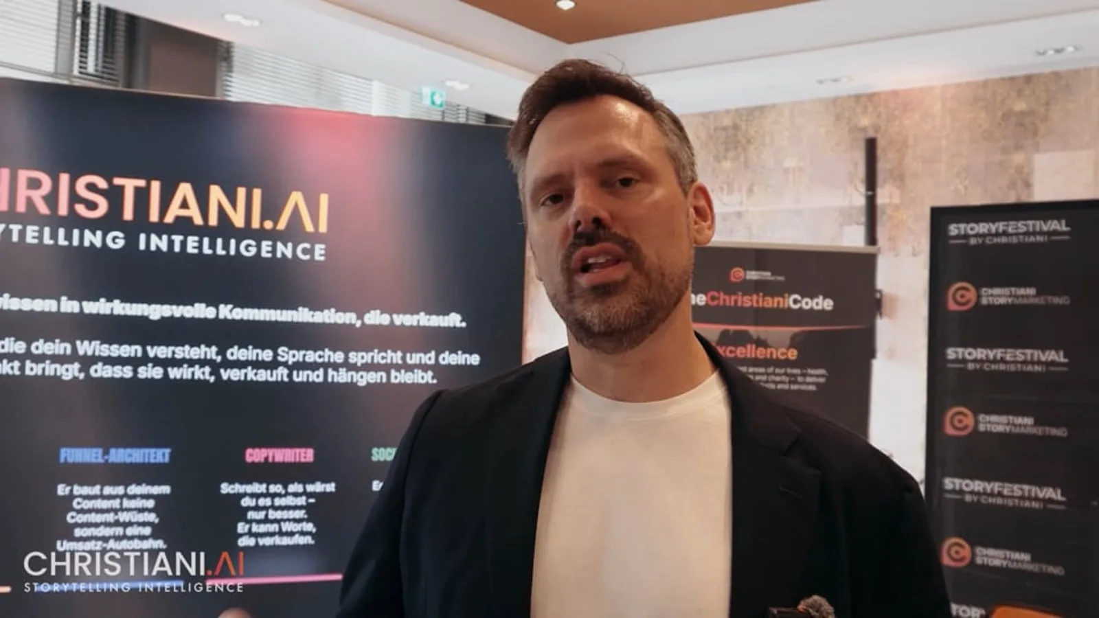 Mann in dunklem Blazer und weißem Shirt vor StoryFestival-Banner spricht vor Publikum