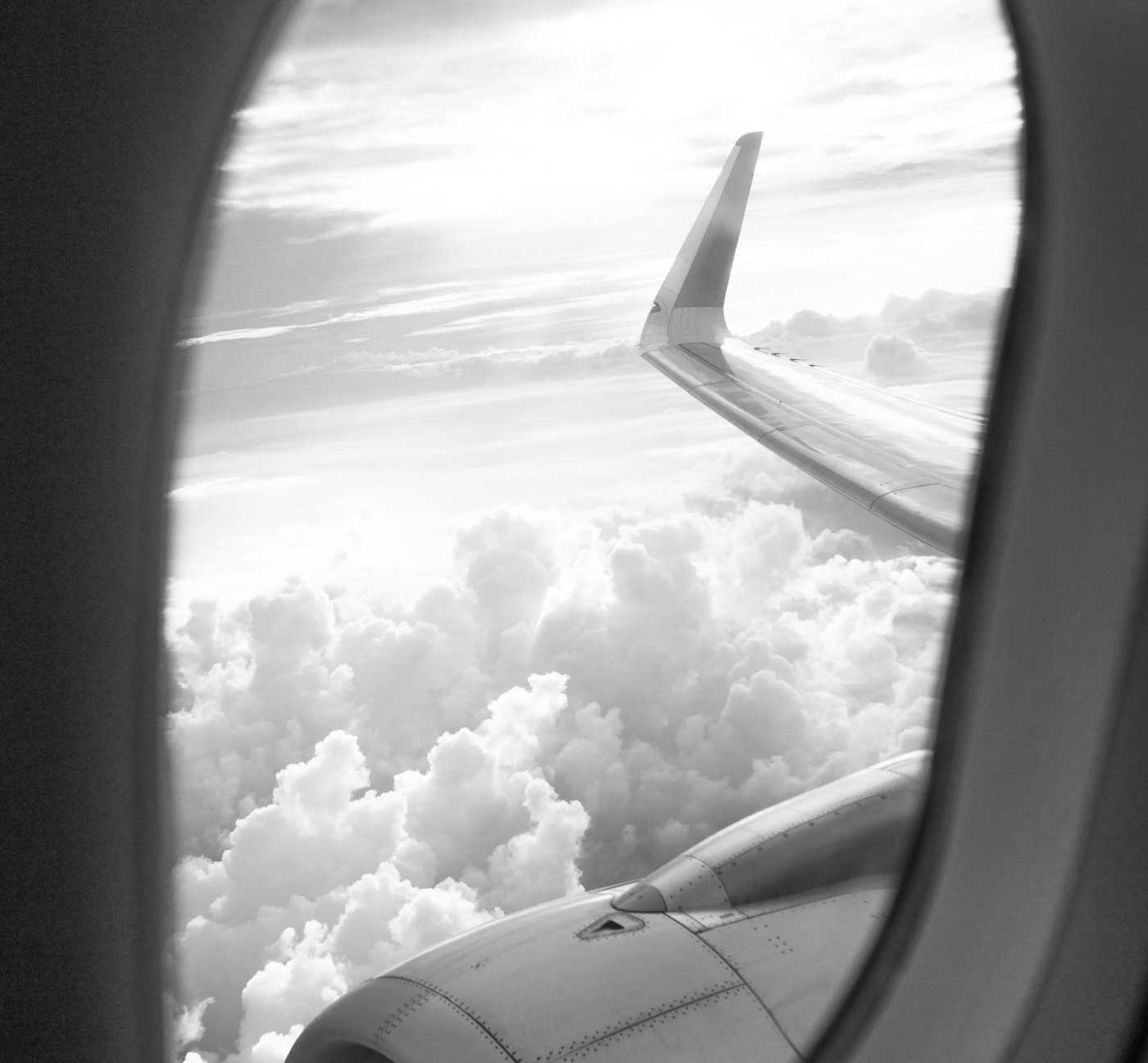 Schwarzweiß-Ausblick aus Flugzeugfenster mit Tragfläche über Wolken