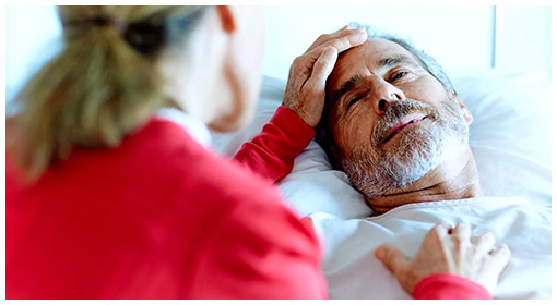 Älterer Patient im Krankenhausbett mit Pflegerin oder Besucherin