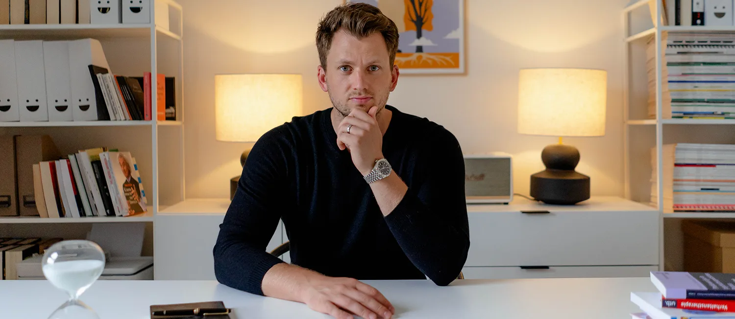 Fotografie von Mario Grabner am Schreibtisch in dunklem Blazer im modernen Büro mit Bücherregalen
