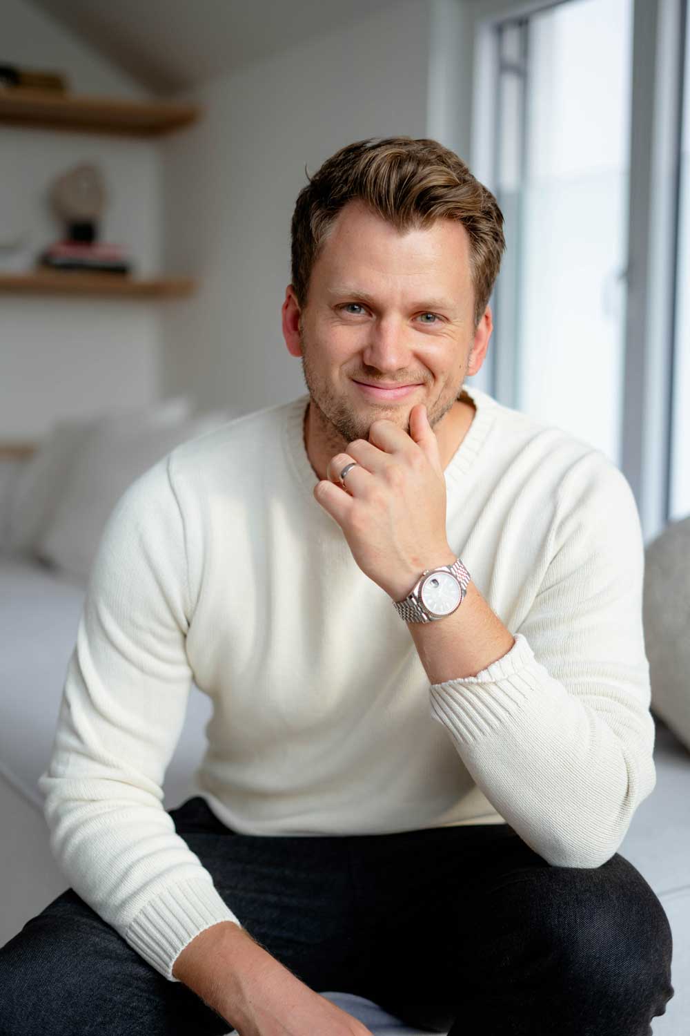 Portrait-Fotografie von Mario Grabner, Mann mit braunem Haar in Weiß-Pullover am Fenster, nachdenkliche Pose