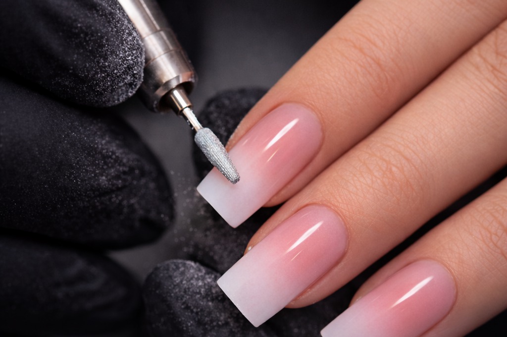 Nageltechniker mit E-File bearbeitet rosa-weißen Ombre-Nagel in quadratischer Form