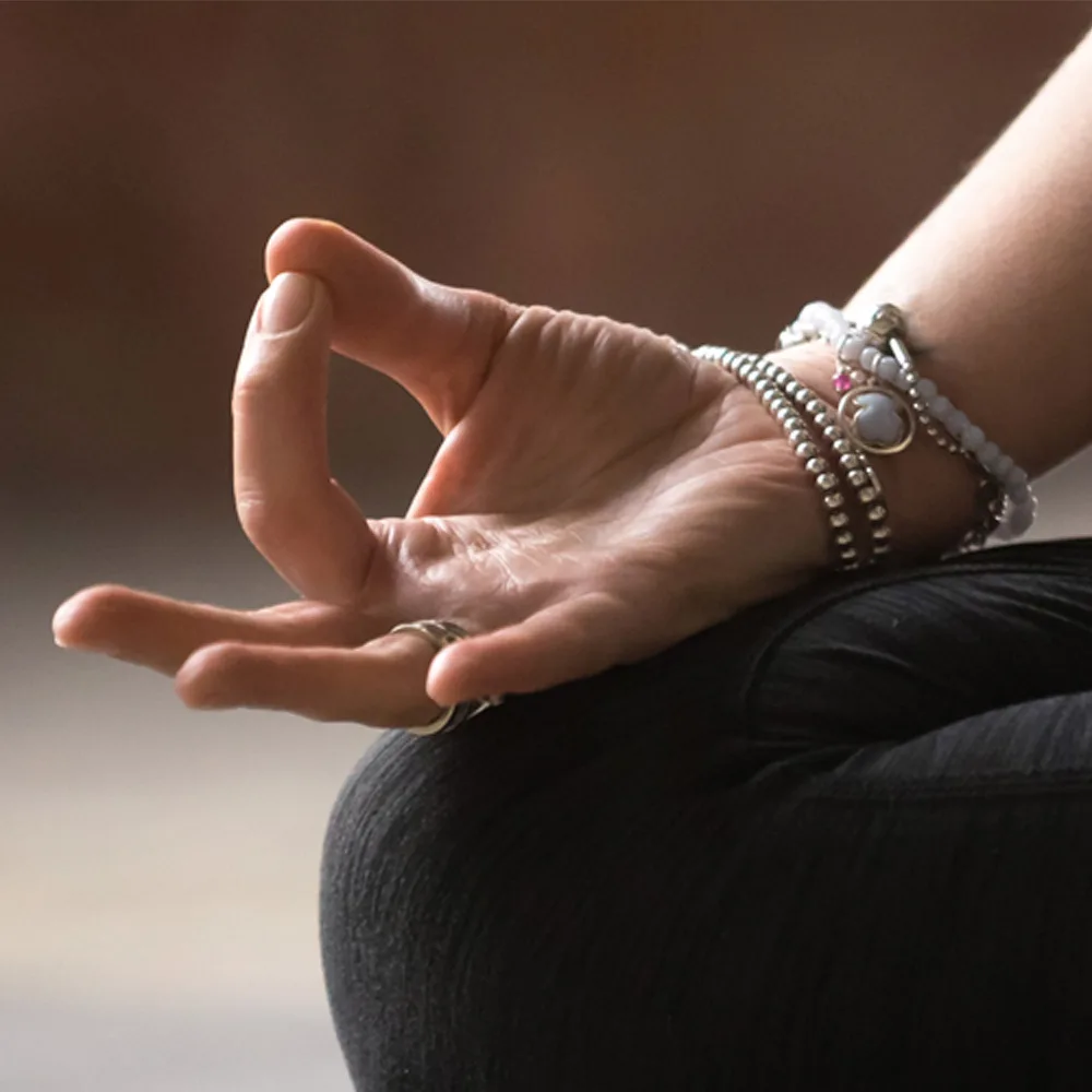 Frauenhände in Mudra-Position mit silbernen Perlenarmband auf schwarzem Stoff