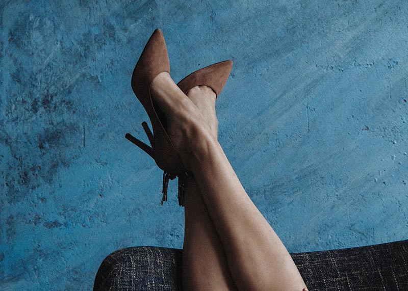 Frauenbein mit braunem High Heel vor blauer Wand