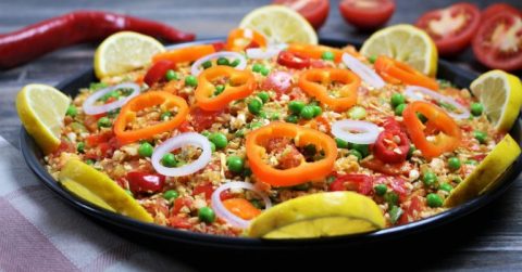 Würzige spanische Paella mit Paprika, Limette und Kräutern auf gelbem Teller