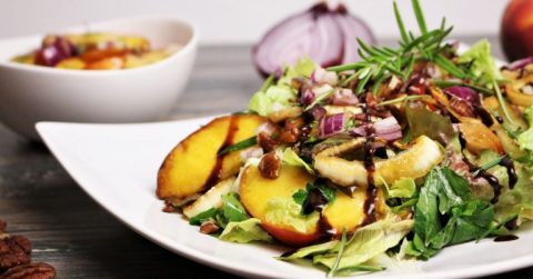 Salat mit marinierten Rosmarin-Pfirsichen, Gemüse und Zwiebeln auf weißem Teller