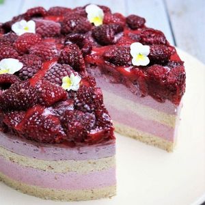 Himbeerbisquittorte mit Himbeeren, Creme-Schichten und weißen Blüten als Dekoration