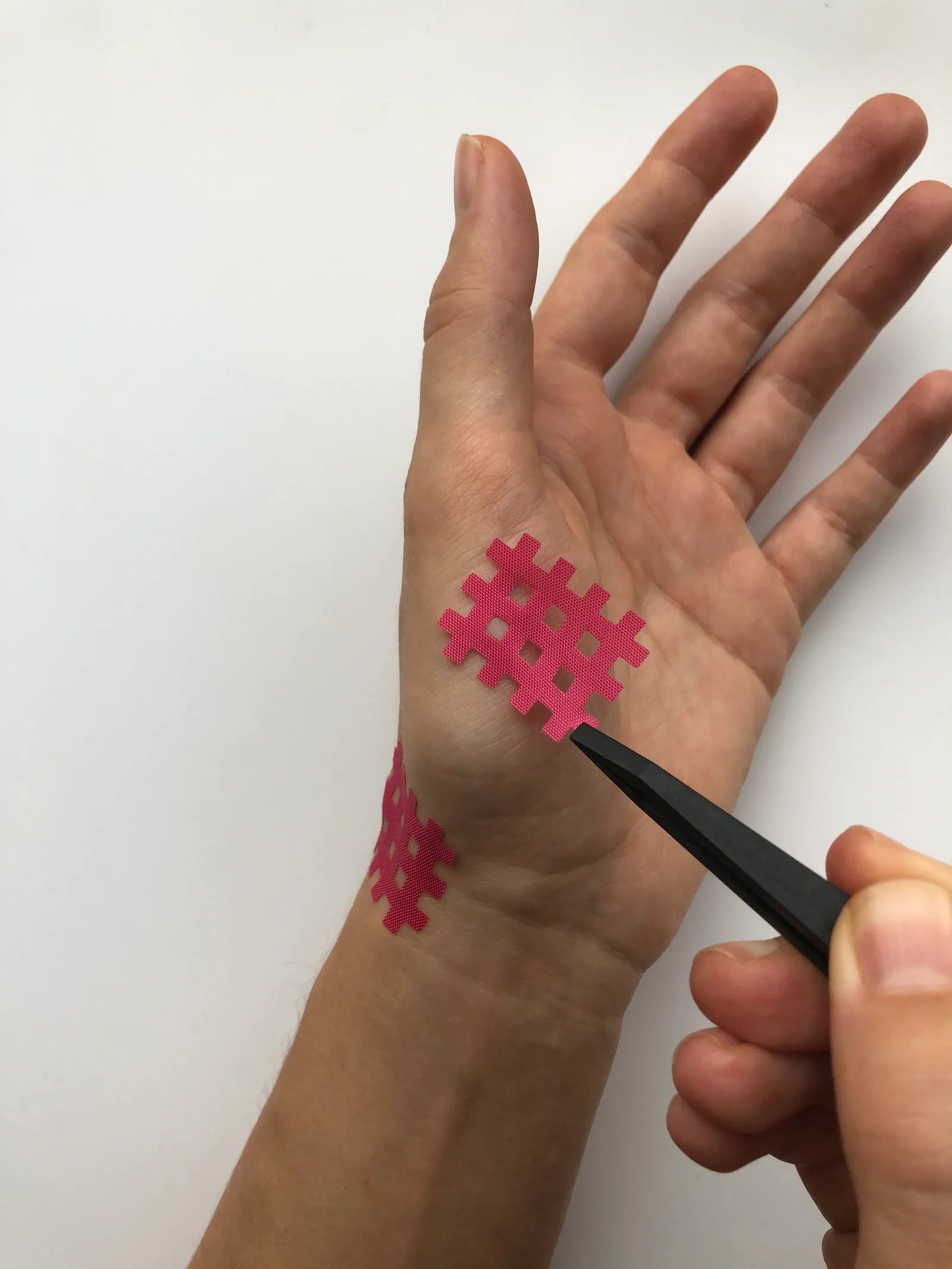 Hand mit roten Kinesio-Tapes in Gitternetz-Muster und therapeutischem Werkzeug