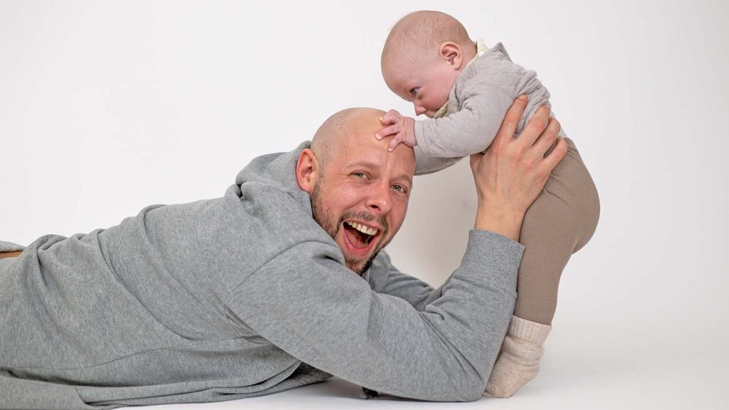 Vater liegt auf dem Boden und hält lachend sein Kleinkind hoch