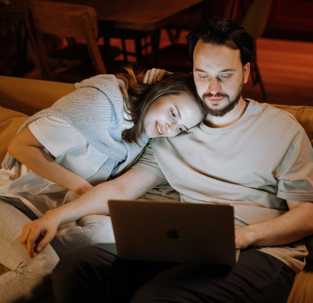 Paar sitzt auf Sofa und schaut gemeinsam auf Laptop-Bildschirm