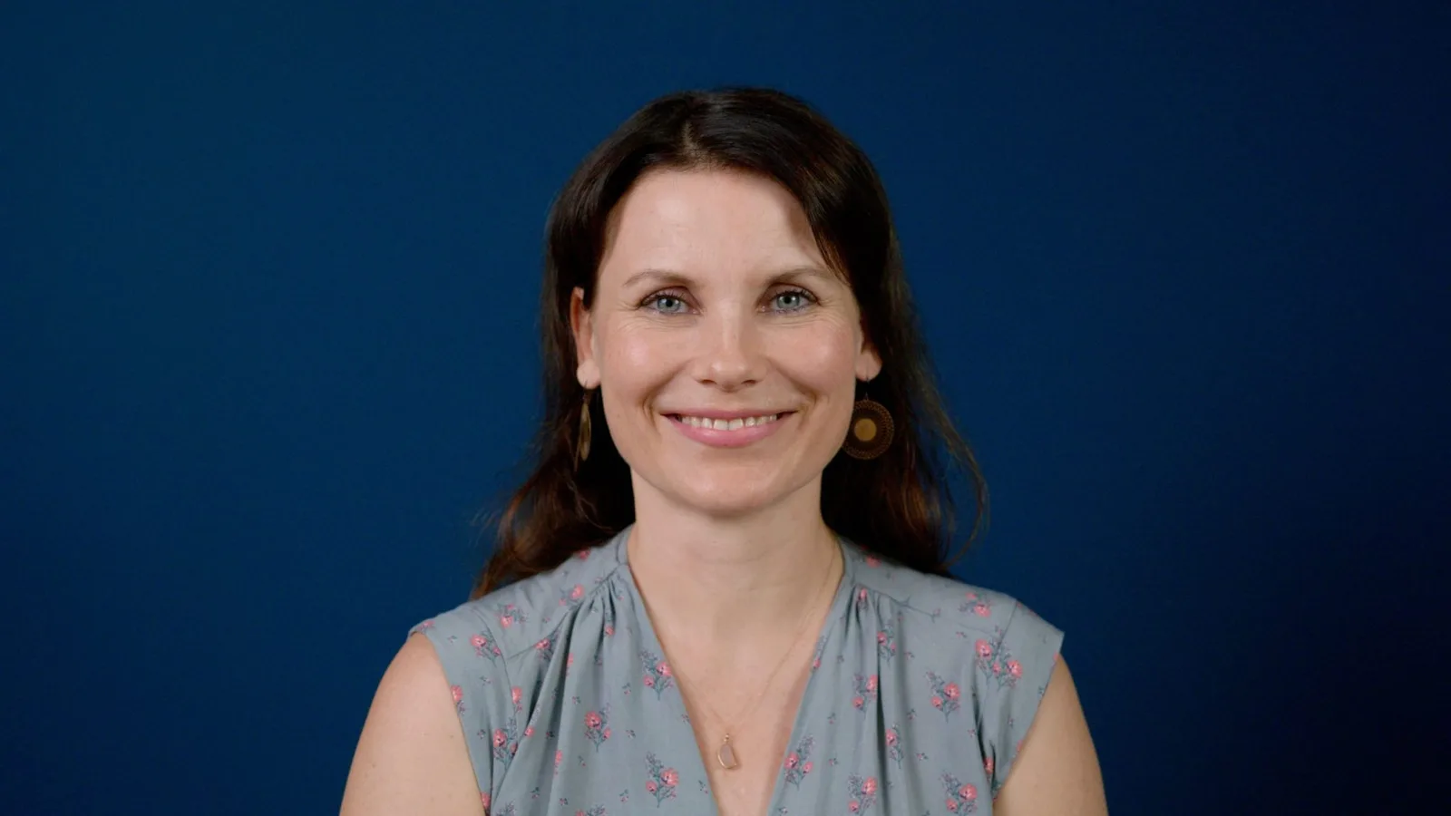 Frau mit dunklen Haaren vor blauem Hintergrund, freundlicher Blick