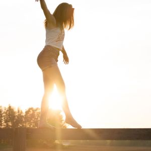 Frau springt bei Sonnenaufgang mit ausgebreiteten Armen in die Luft