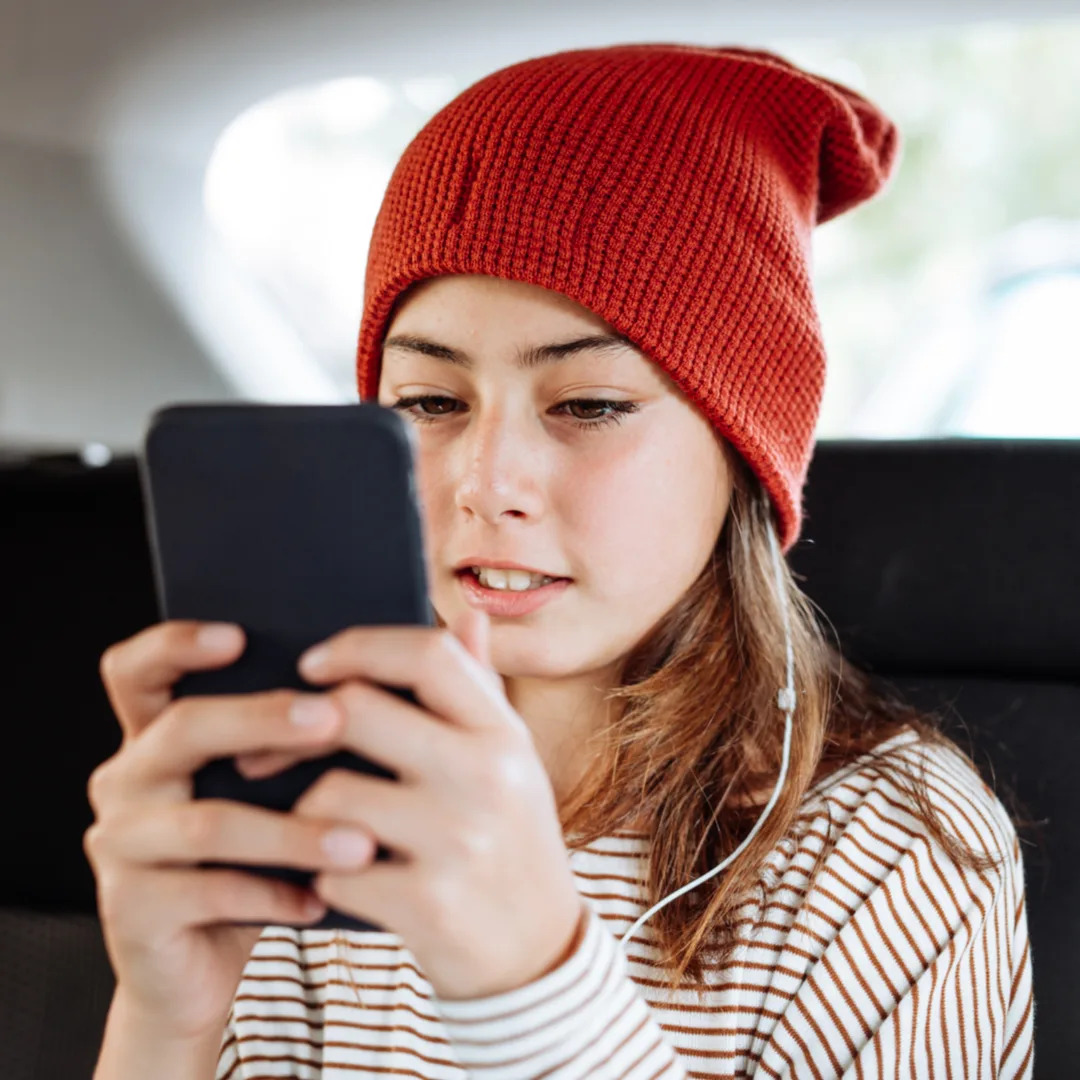 Teenager mit roter Mütze schaut lächelnd auf Smartphone mit Kopfhörern