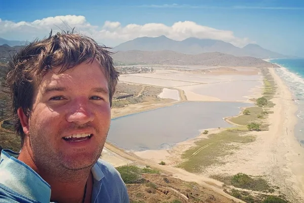 Christoph Heuermann lächelnd vor Landschaftspanorama mit Strand und Bergen