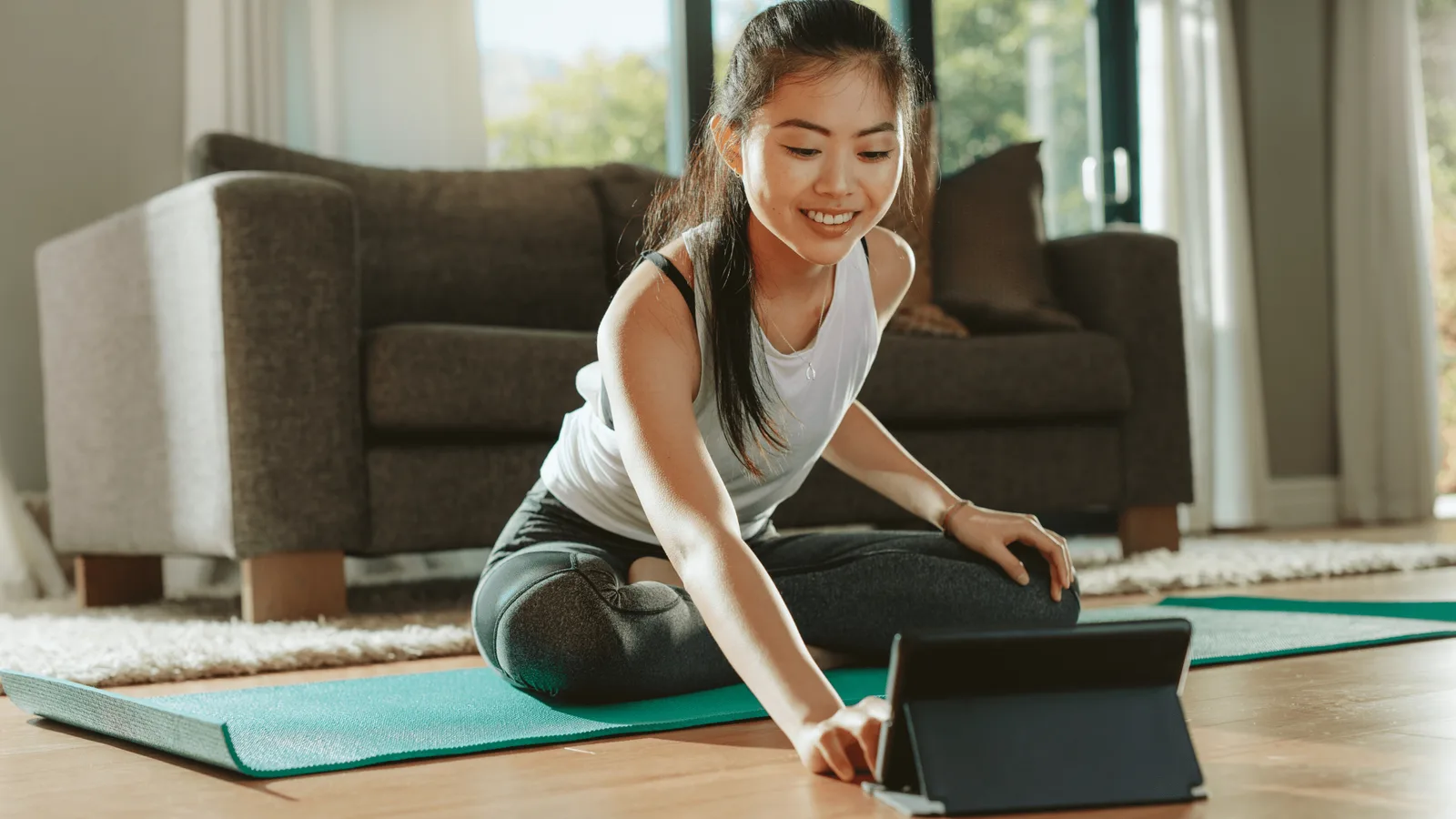 Junge Frau beim Online-Fitnesstraining auf Yogamatte im Wohnzimmer