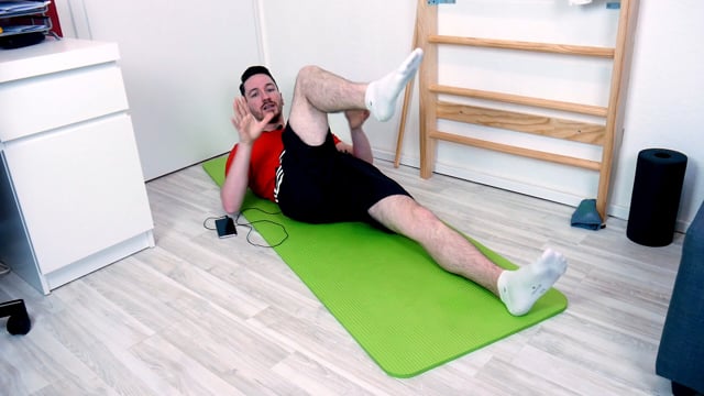Mann in rotem Shirt führt Bauchmuskelübung auf grüner Trainingsmatte aus
