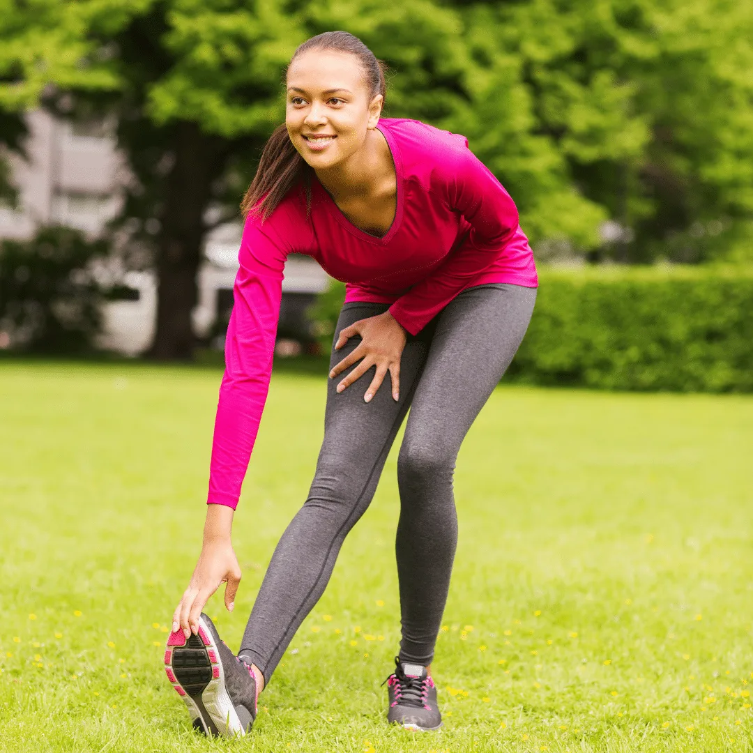 Frau in pinkem Shirt und grauer Leggings in Trainingsposition auf grünem Rasen