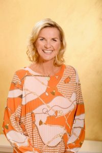 Portrait einer lächelnden Frau mit blondem Haar vor gelbem Hintergrund