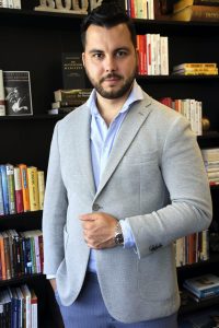 Porträt eines Mannes in hellblauem Hemd und grauem Blazer vor Bücherregal
