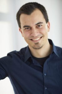 Portrait eines jungen Mannes mit dunklem Haar und Lächeln vor hellem Hintergrund