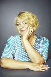 Portrait einer Frau mit blondem Haar und Hand am Gesicht vor grauem Hintergrund