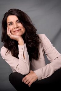 Portrait einer Frau mit langen dunklen Haaren vor grauem Hintergrund