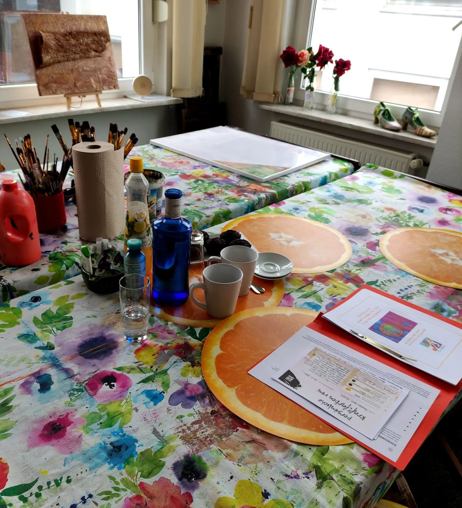 Arbeitsplatz im Atelier mit Farbmustern, Pinseln, Blumen und Coaching-Unterlagen