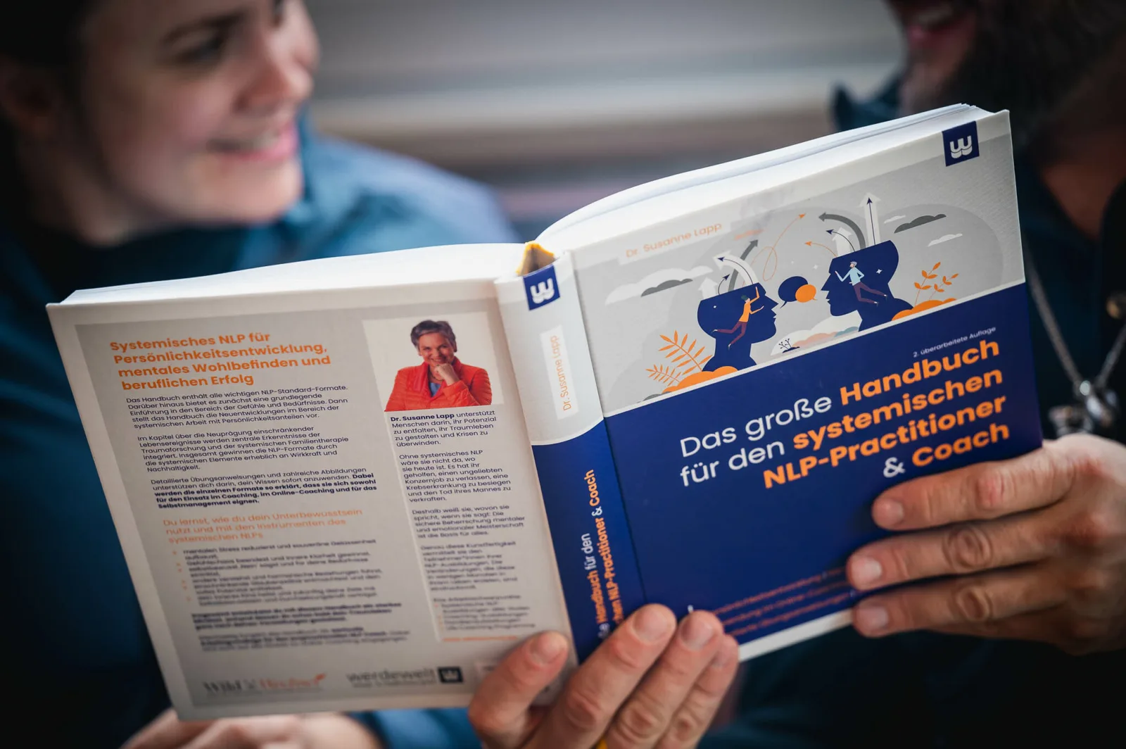 Das große Handbuch für den systemischen NLP-Practitioner 7 Fotografie: Hände halten aufgeschlagenes Buch mit Cover-Illustration und innerem Inhaltstext, Portrait-Format