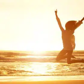 Frau mit erhobenen Armen bei Sonnenaufgang am Strand, Lebensgestaltung und Erfolg