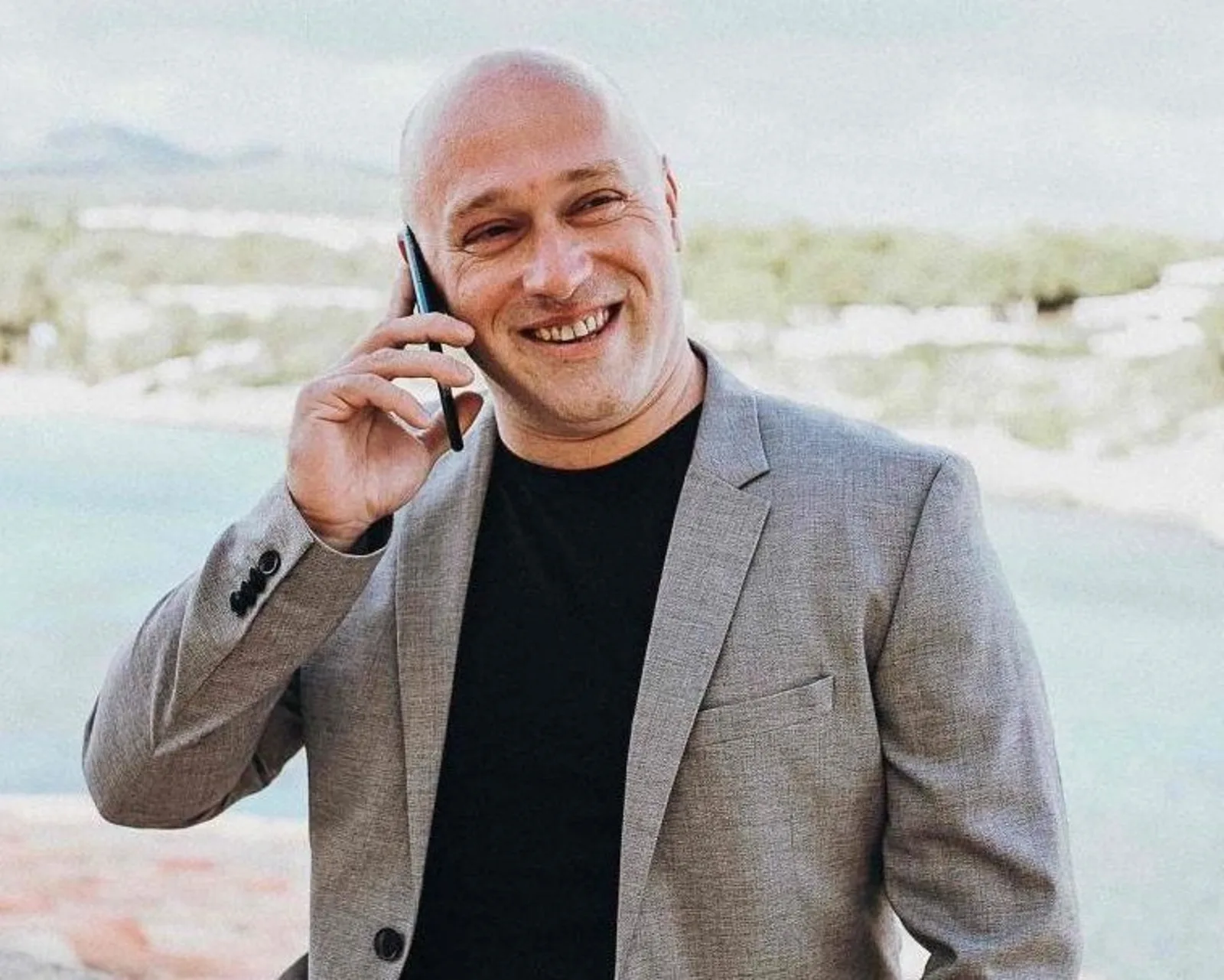 Portrait von Danny Adams am Telefon in Blazer vor Landschaftshintergrund