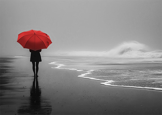 Person mit rotem Regenschirm am Strand, Schwarzweißfoto mit Farbakzent