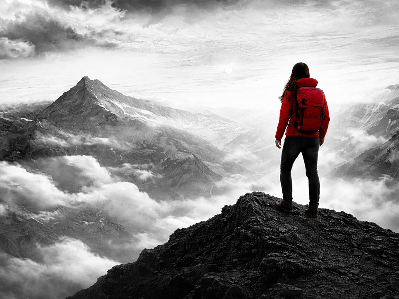 Wanderer mit rotem Rucksack auf Gebirgspfad mit Bergpanorama und Nebel