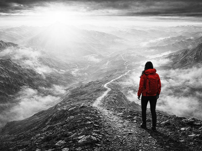 Wanderer in roter Jacke auf Bergkamm mit Tal und Wolken im Hintergrund