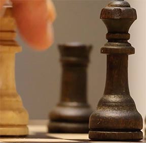 Schachfiguren in Schwarz und Weiß, Nahaufnahme einer dunklen Bischofsfigur im Fokus