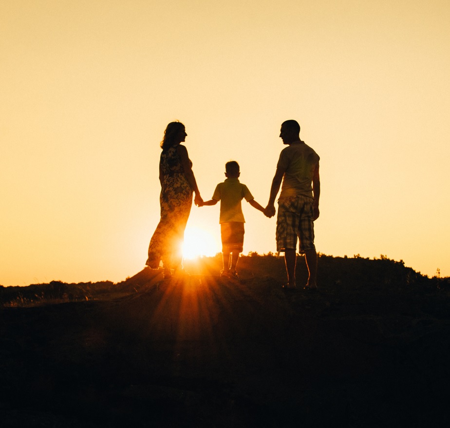 Silhouetten einer Familie bei Sonnenaufgang auf einem Hügel, Hände haltend, warm beleuchteter Himmel