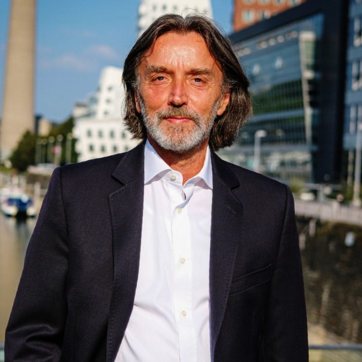 Porträt von Joachim Gerlach mit langen Haaren vor urbaner Kulisse