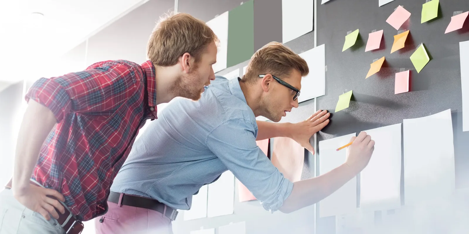 Zwei Männer ordnen bunte Notizzettel an Wand mit Brainstorming-Konzept