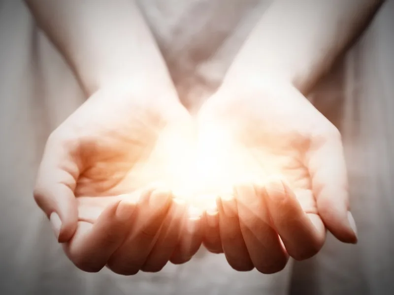 Hände einer jungen Frau mit leuchtendem Licht in der Mitte, symbolisiert Teilen, Geben und Schutz