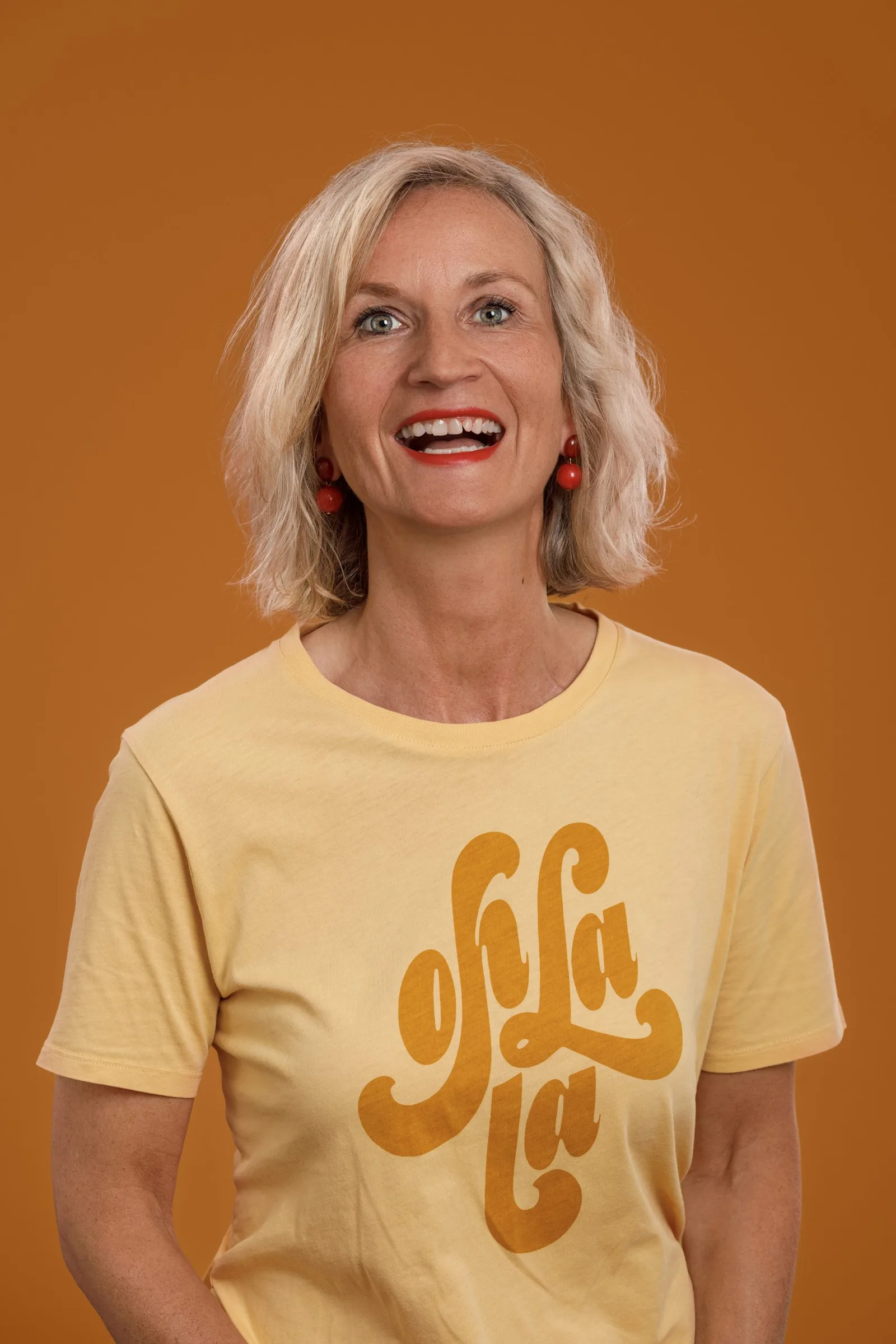 Porträt von Nina Binvel in gelbem ohlàlà T-Shirt vor orange-gelbem Hintergrund lächelnd