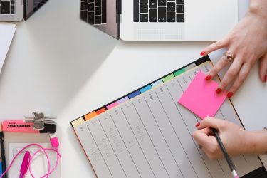 Schreibtisch von oben mit Laptop, Kalender, Notizbuch und bunten Stickern zur Zeitplanung