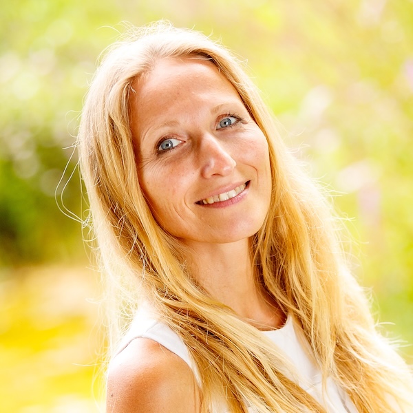 Jana Iger, blonde Frau in weißem Oberteil vor gelbgrünem Bokeh-Hintergrund