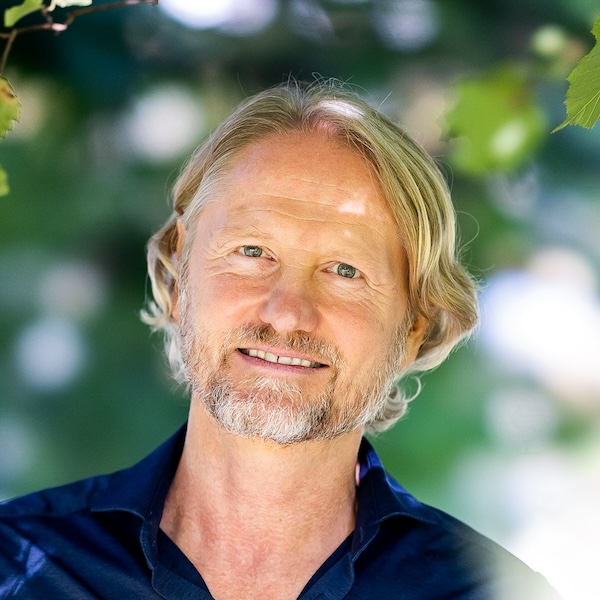Steffen Lohrer lächelt in die Kamera, blonde Haare, dunkles Hemd, unscharfer grüner Hintergrund
